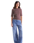 A model wearing a short-sleeve crewneck top with dark red and white horizontal stripes, paired with wide-leg blue jeans, standing against a light gray studio background.