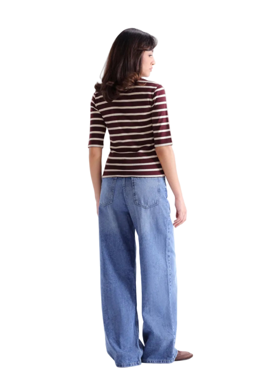 A woman shown from the back wearing a brown and white striped short-sleeve top and wide-leg blue jeans, standing against a light gray studio background.